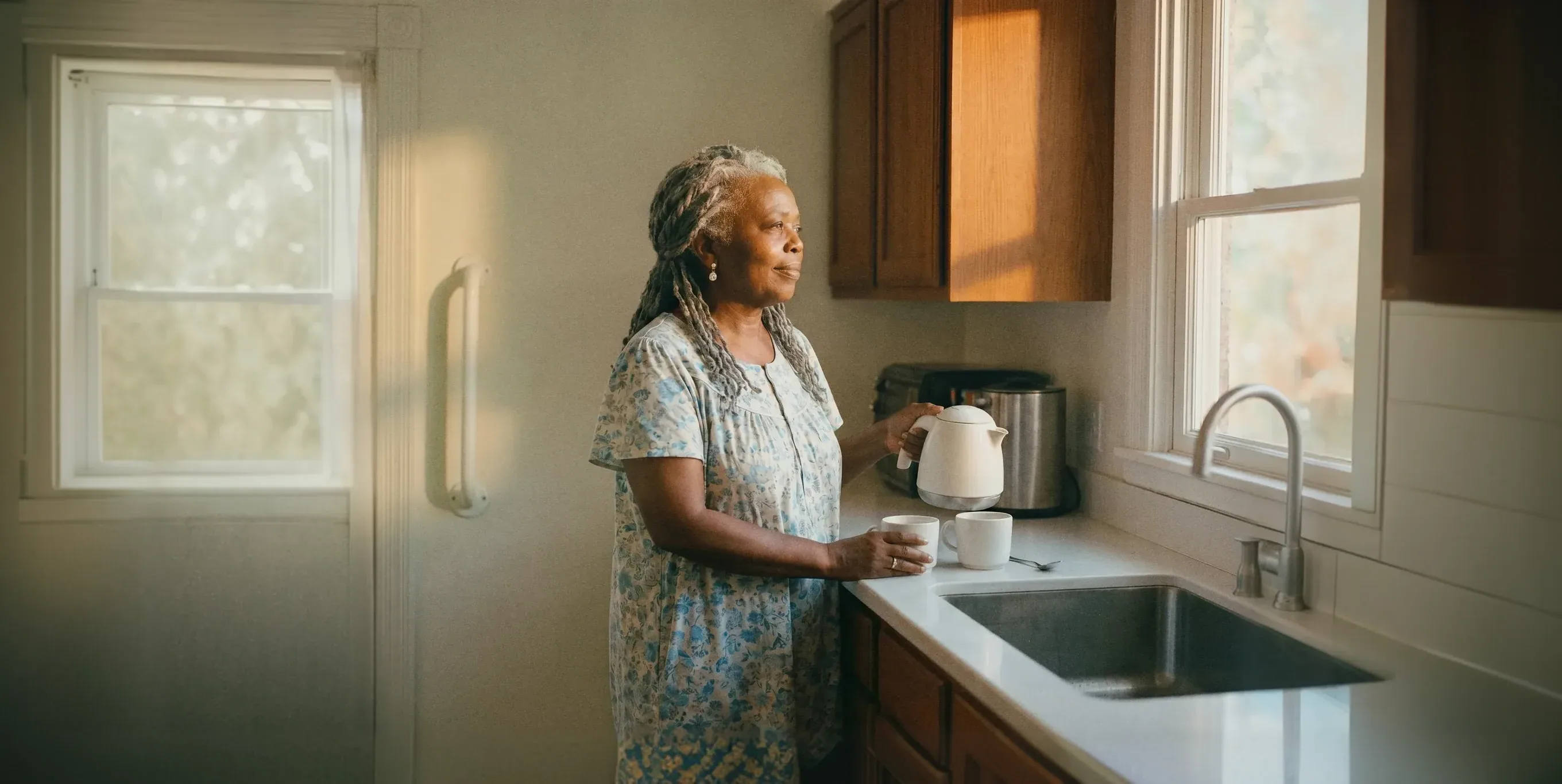 A woman pouring tea at her kitchen sink, looking out of the window