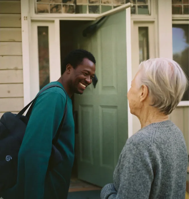 A care worker greeting an older woman at her front door
